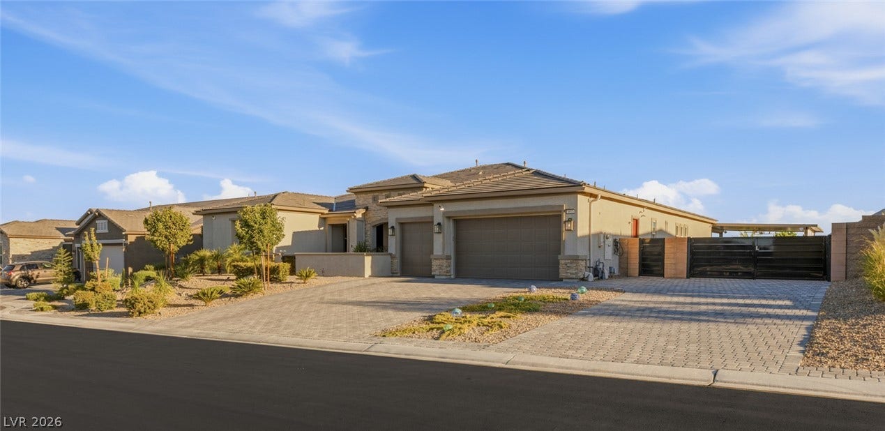 An expansive paver driveway leads to a modern exterior with stone accents and tile roofing.
