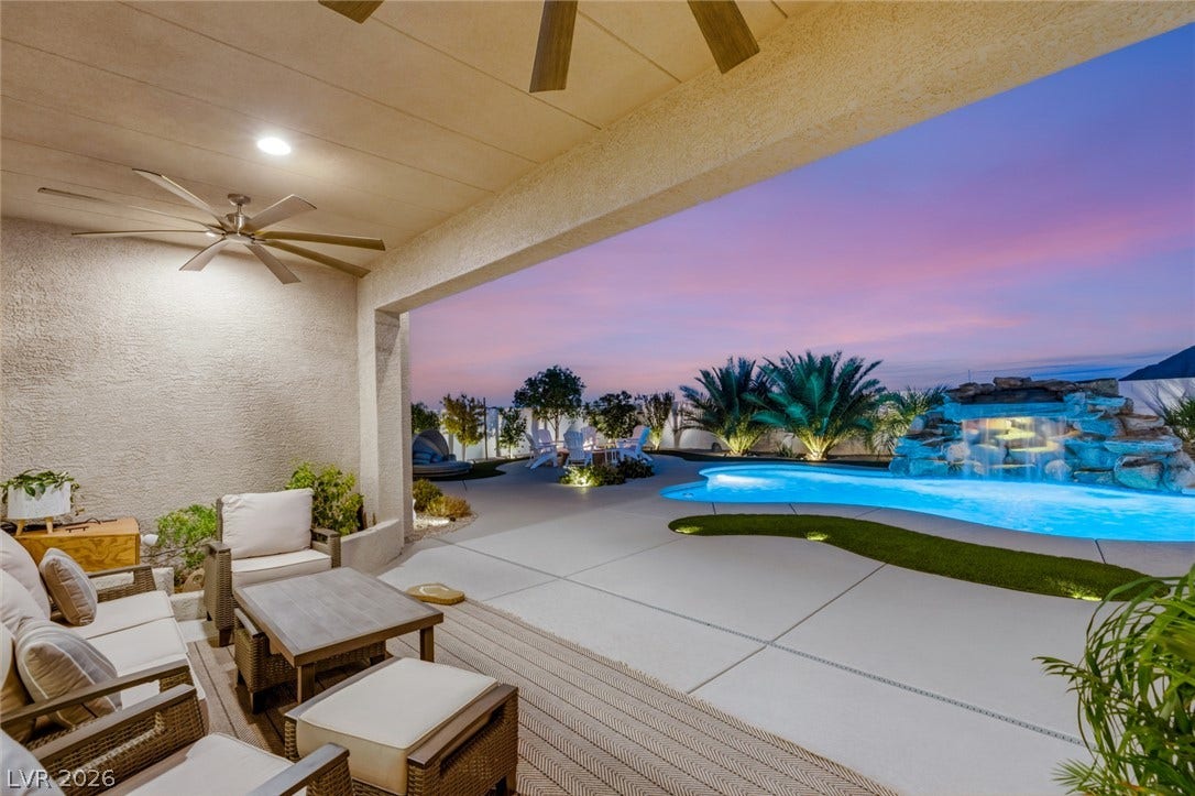 An inviting covered patio steps out to a pristine concrete pool deck and rock waterfall.