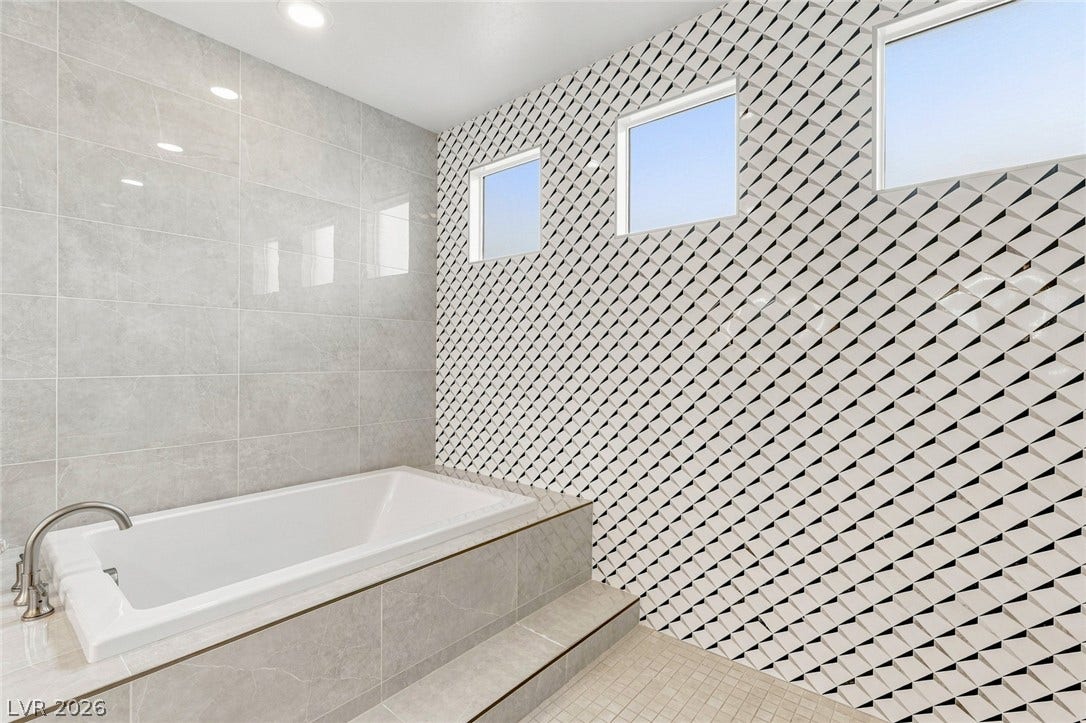High-placed windows invite natural light over a modern soaking tub framed by geometric tilework.