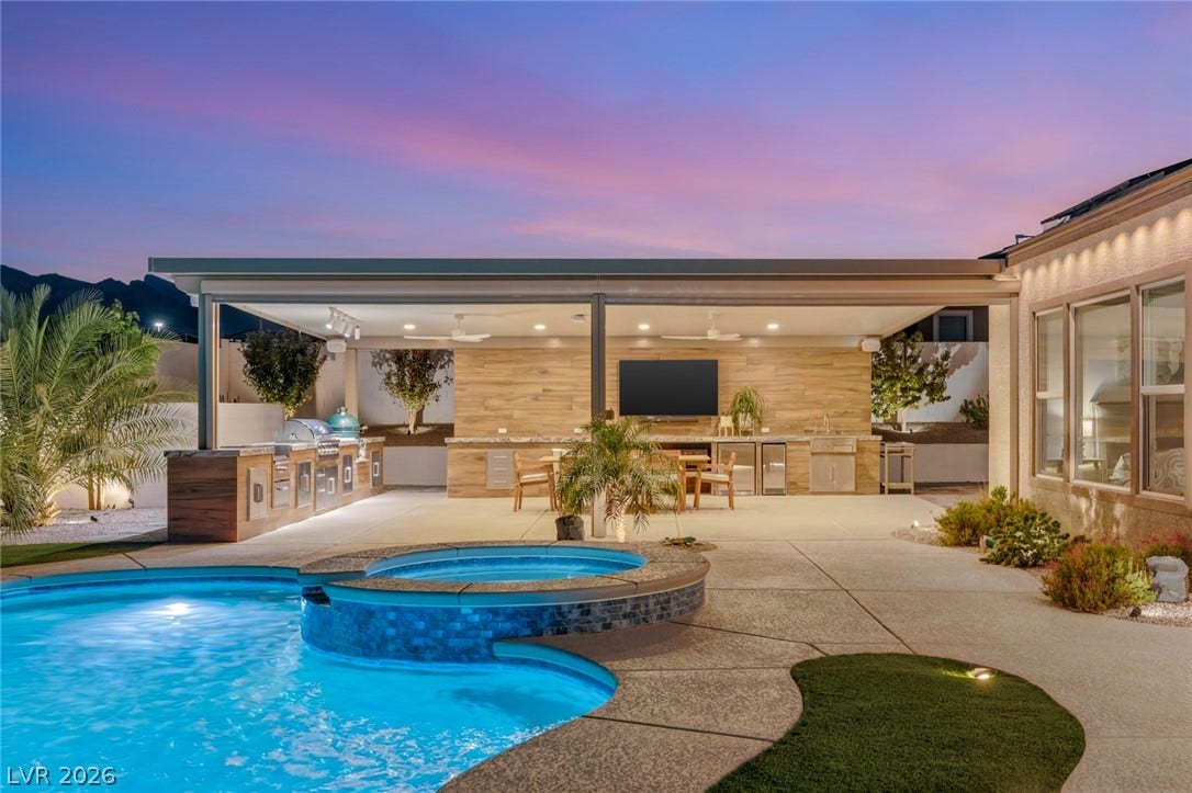 An inviting backyard oasis features a gleaming pool and spa alongside a covered outdoor kitchen.