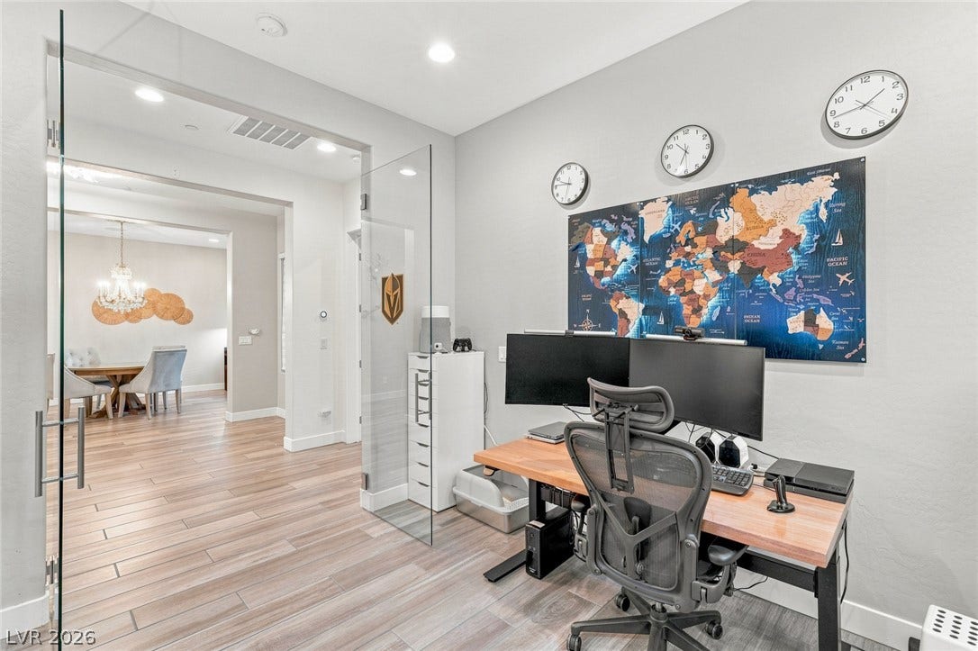 Double glass doors enclose a quiet workspace featuring modern recessed lighting and handsome wood-look flooring.