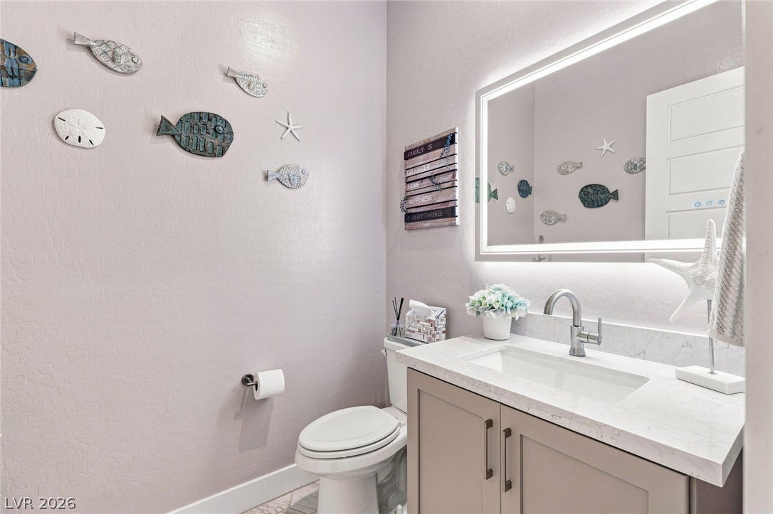 Smooth stone countertops and a backlit vanity mirror elevate this modern powder room.