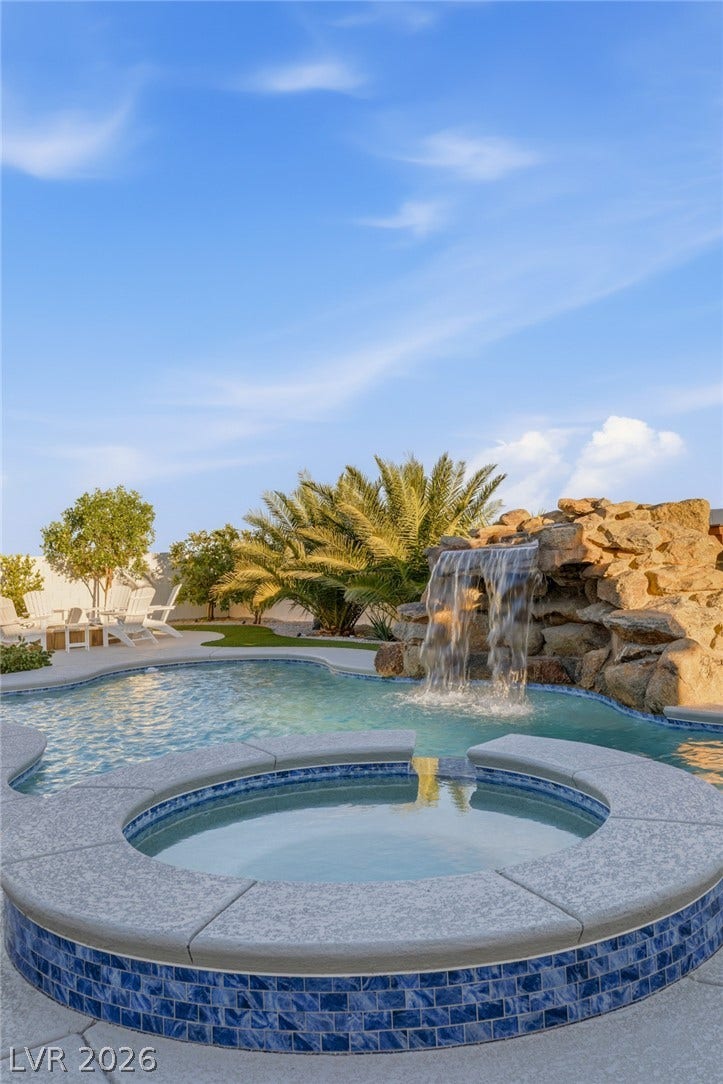 An elevated spa spills directly into a sparkling swimming pool anchored by a stone waterfall.