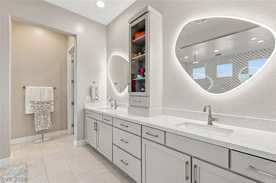 Custom cabinetry and stone countertops anchor this modern double vanity with backlit mirrors.