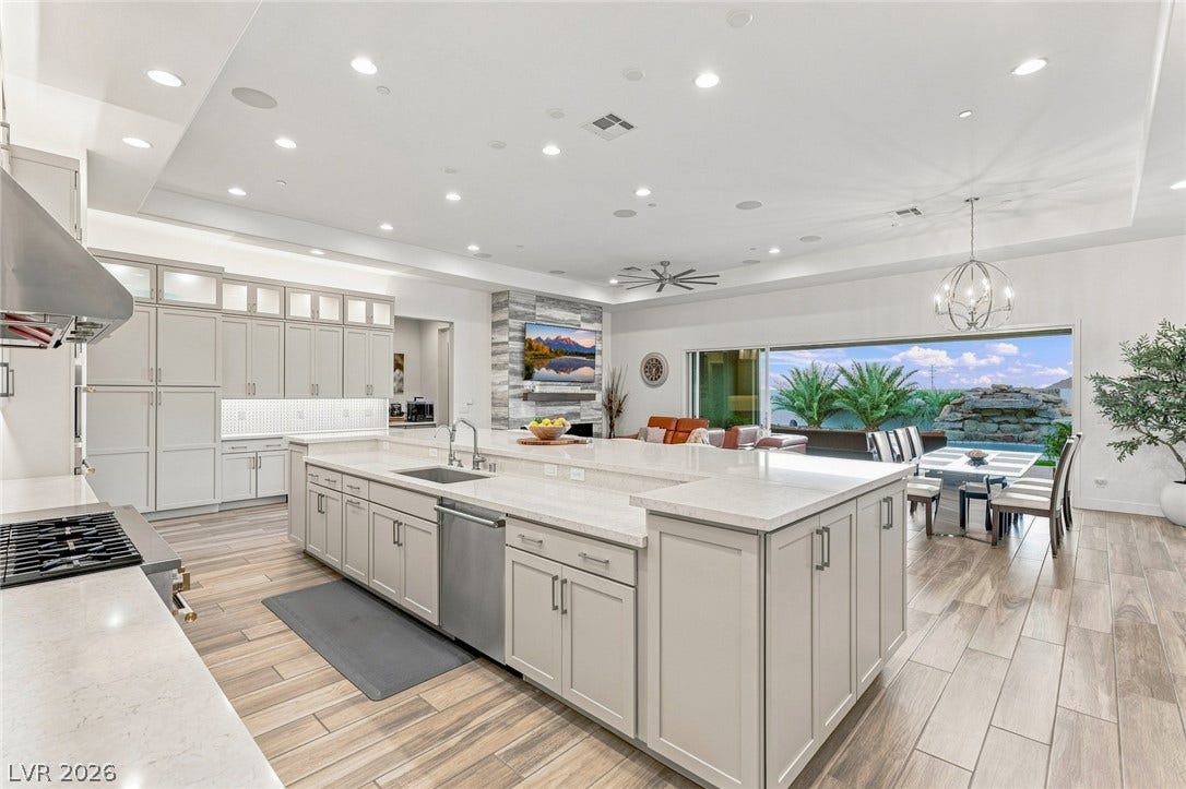 Recessed lighting illuminates this expansive open kitchen showcasing a massive central island and wood-look flooring.