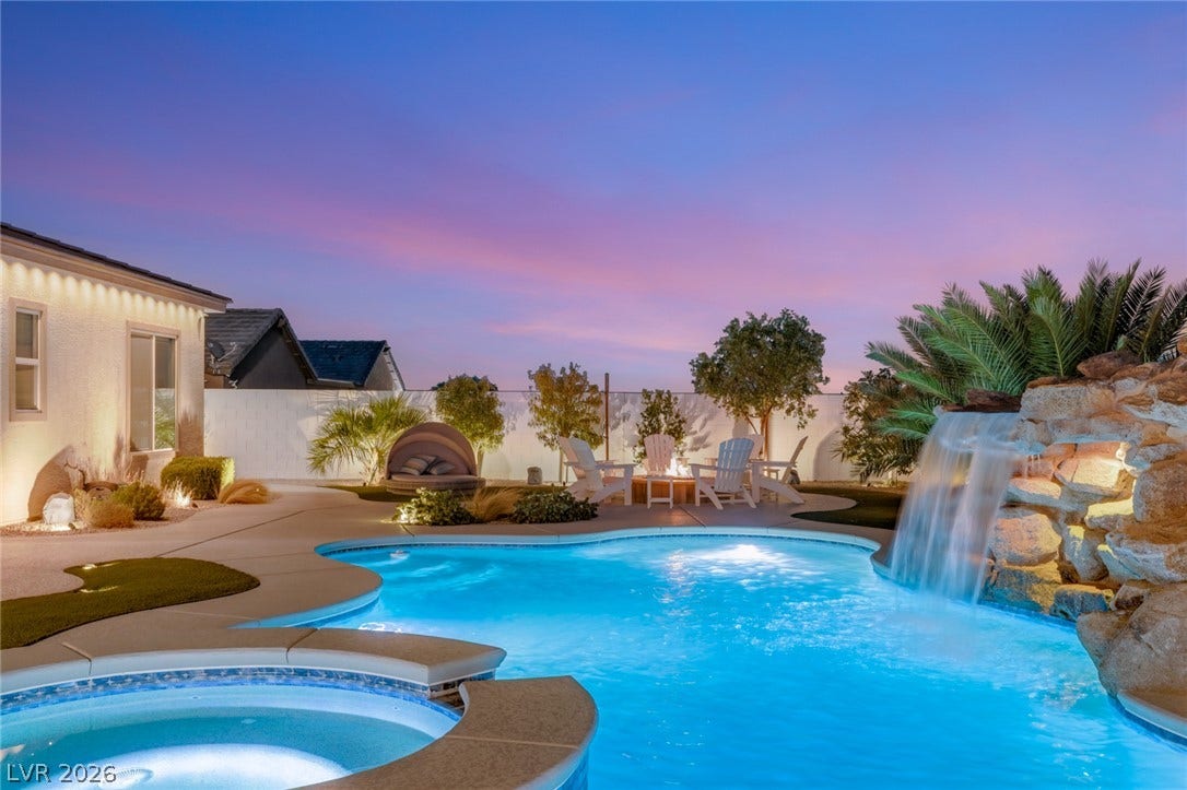An inviting backyard oasis features a glistening swimming pool and a stone waterfall feature.