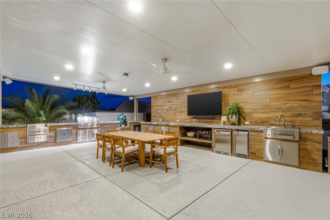 An expansive covered patio showcases a fully equipped outdoor kitchen and durable concrete flooring.