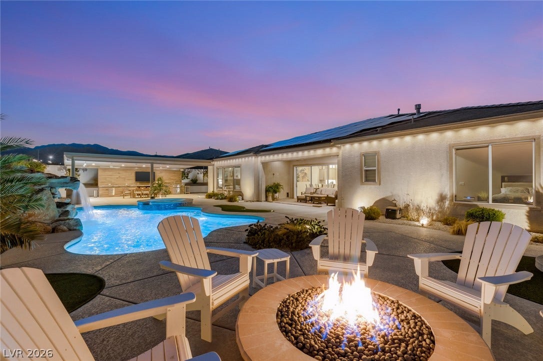 An inviting fire pit sits adjacent to a glowing swimming pool under twilight skies.