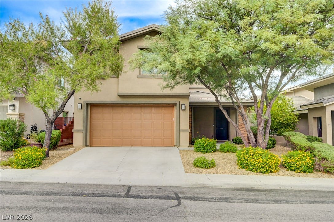 5608 Beckett Hill Court, Las Vegas, NV 89135 Lush desert plantings frame a two-story residence featuring a paved driveway and stucco exterior.