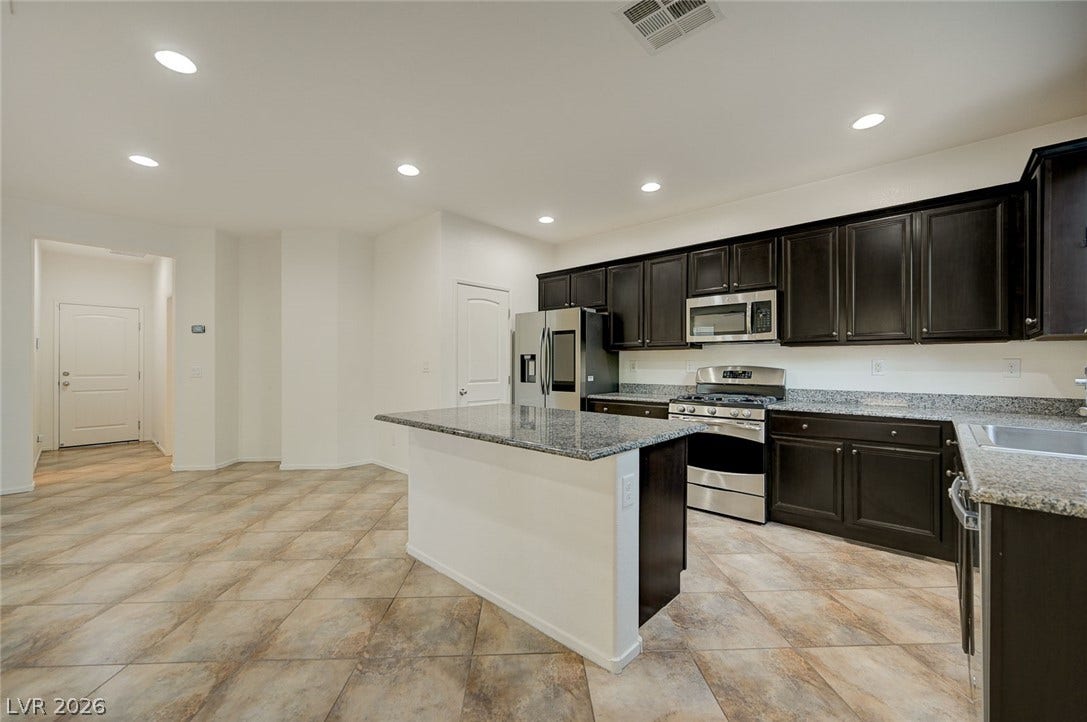 5608 Beckett Hill Court, Las Vegas, NV 89135 Dark cabinetry and granite counters define this kitchen, opening directly to a spacious tile-floored area.
