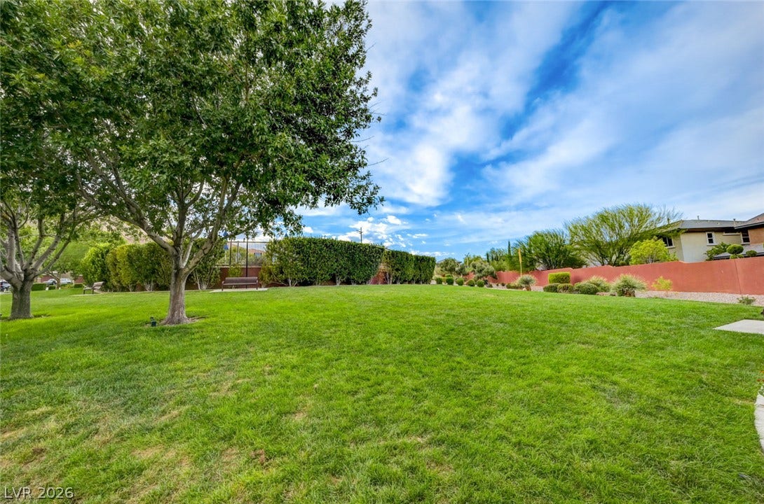 5608 Beckett Hill Court, Las Vegas, NV 89135 Mature trees shade a manicured lawn bordered by privacy hedges under blue skies.