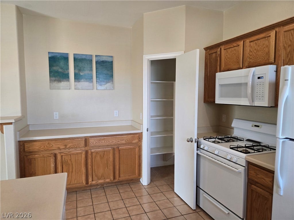 5935 Nuevo Leon Street, #2, North Las Vegas, NV 89031 A functional kitchen features warm wood cabinetry, ceramic tile flooring, and a walk-in storage pantry.