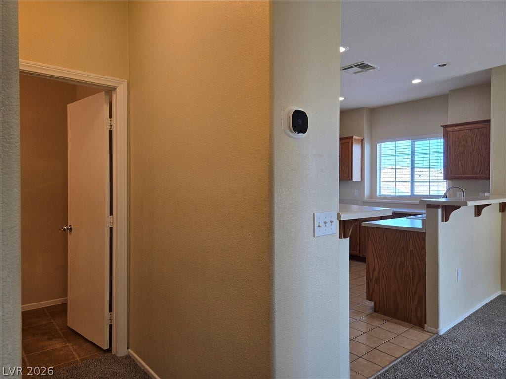 5935 Nuevo Leon Street, #2, North Las Vegas, NV 89031 An open doorway leads from carpeted floors into a kitchen with classic wood cabinetry.