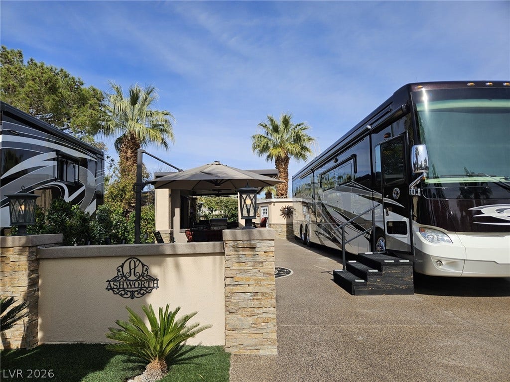 8175 Arville Street, #287, Las Vegas, NV 89139 Palm trees frame a paved parking pad featuring stone pillars and a sheltered seating area.