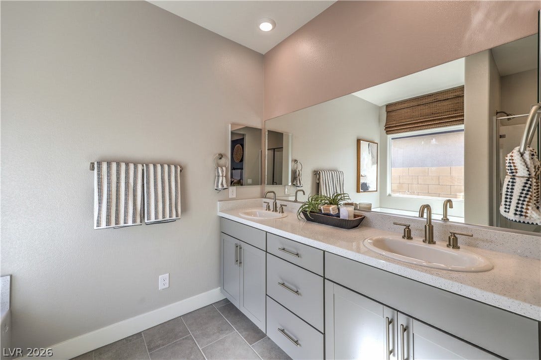 1044 Gentle Swan Street, Henderson, NV 89011 A sleek double vanity with stone countertops anchors this modern, light-filled bathroom. Photo is of actual model home for sale.