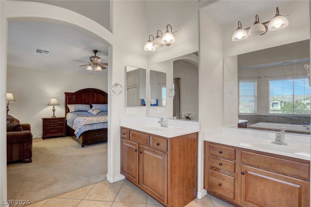 5508 Meridian Rain Street, North Las Vegas, NV 89031 An arched opening connects the carpeted suite to a bathroom featuring wood vanities and tile flooring.