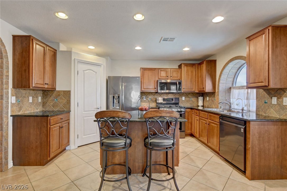 5508 Meridian Rain Street, North Las Vegas, NV 89031 Warm wood cabinetry and granite countertops frame a functional central island with breakfast bar seating.