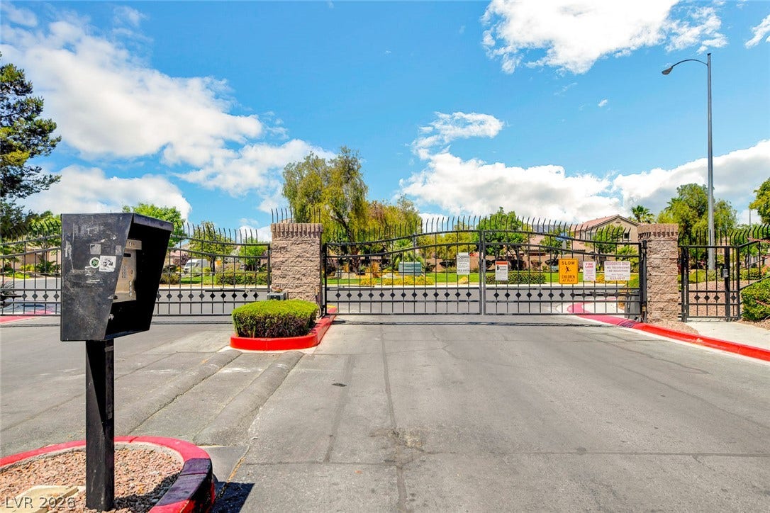 5508 Meridian Rain Street, North Las Vegas, NV 89031 A secure gated entrance features stone pillars and wrought iron gates under a blue sky.