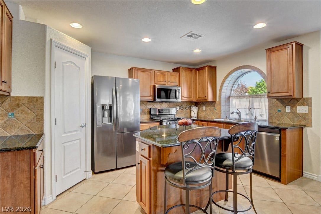 5508 Meridian Rain Street, North Las Vegas, NV 89031 Rich wood cabinetry and stone counters anchor this bright workspace with a central island.