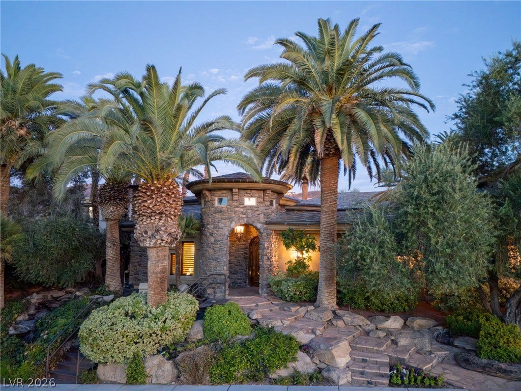 1513 Foothills Village Drive, Henderson, NV 89012 Towering palm trees frame a stone-accented facade and arched entryway.