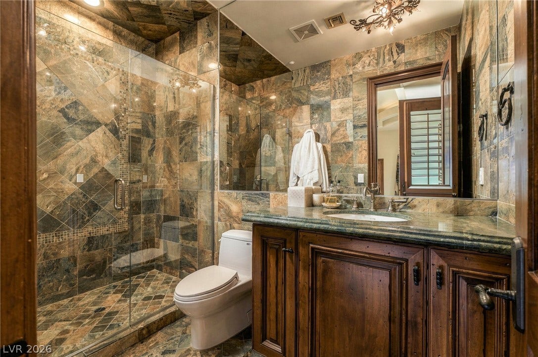 1513 Foothills Village Drive, Henderson, NV 89012 Richly patterned stone tiling creates a cohesive look across this bathroom walls and glass shower.