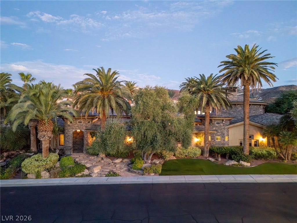 1513 Foothills Village Drive, Henderson, NV 89012 Lush palm trees frame this grand stone estate nestled under a twilight sky.
