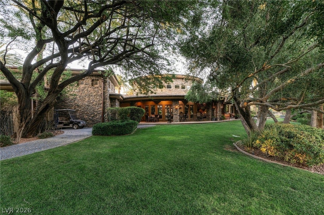 1513 Foothills Village Drive, Henderson, NV 89012 Mature trees shade a manicured lawn leading toward the stone-clad rear exterior of the home.