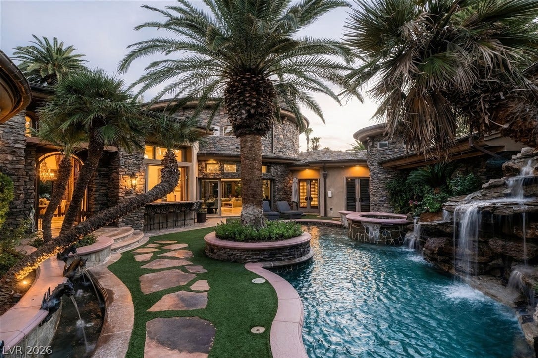 1513 Foothills Village Drive, Henderson, NV 89012 Lush palm trees and stone architecture frame a resort-style swimming pool with cascading waterfalls.
