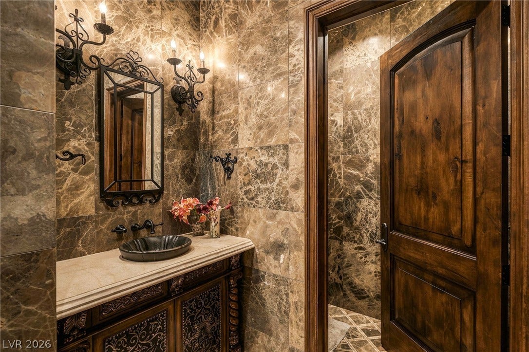 1513 Foothills Village Drive, Henderson, NV 89012 Rich marble tiles wall the powder room, complemented by a rustic wood door.