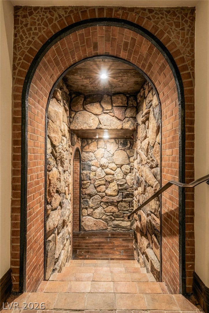 1513 Foothills Village Drive, Henderson, NV 89012 A dramatic arched brick entryway leads down to stone-lined walls and rustic tiled flooring.