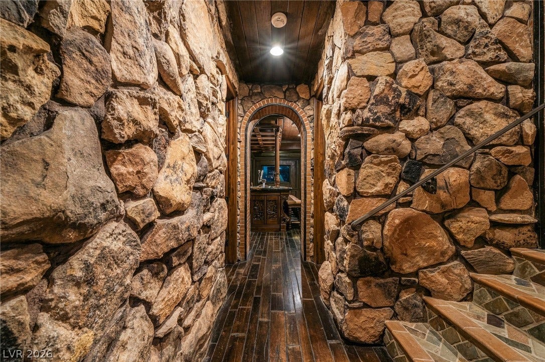 1513 Foothills Village Drive, Henderson, NV 89012 Massive stone walls and dark wood ceilings define this rustic, lodge-inspired hallway.