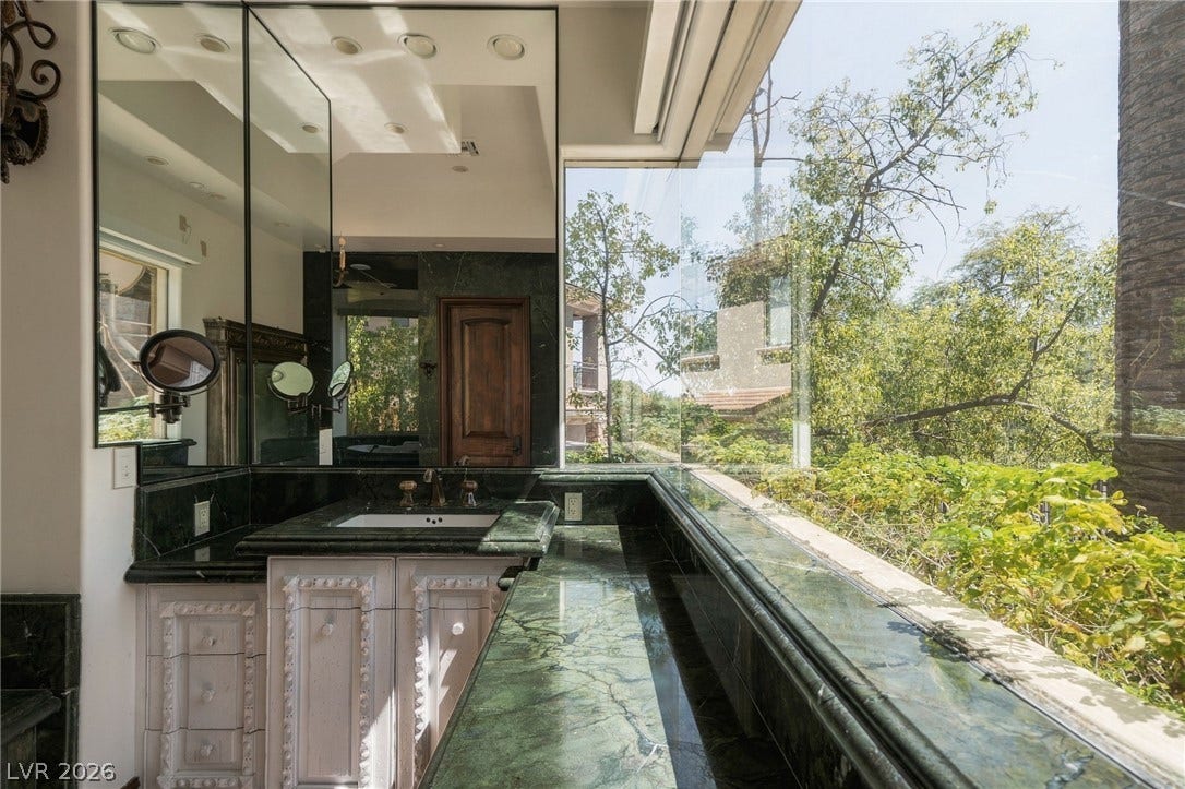 1513 Foothills Village Drive, Henderson, NV 89012 Massive windows frame lush garden views beside the elegant stone-counter vanity.