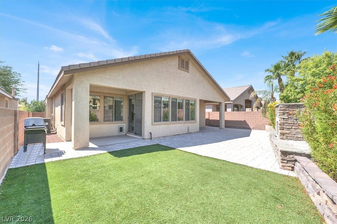 A spacious stone patio and lush green lawn define this private, low-maintenance backyard.
