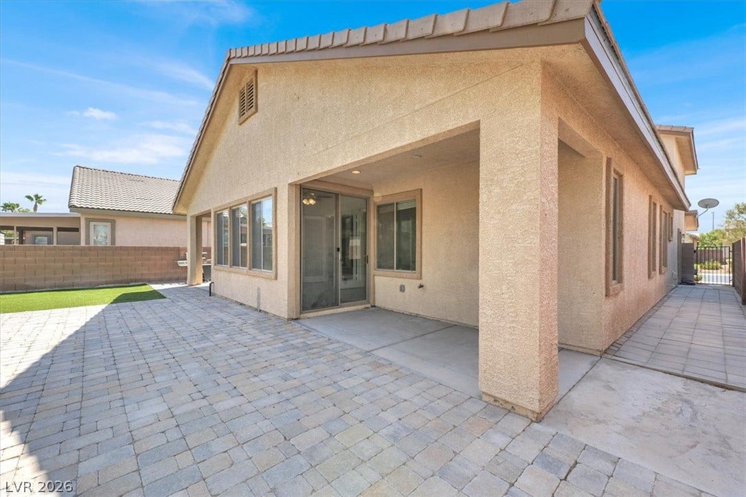 An inviting covered patio opens onto a clean, spacious brick-paved backyard terrace.