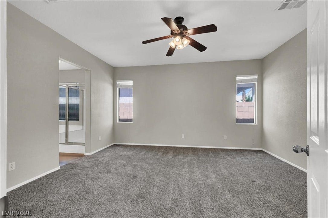 Plush carpeting anchors this spacious bedroom featuring tall windows and a wide open doorway.