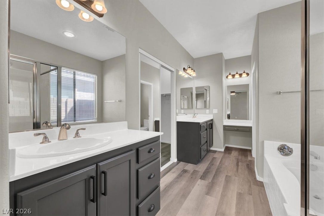 A spacious bathroom features dual dark vanities, wood-look flooring, and a large soaking tub.