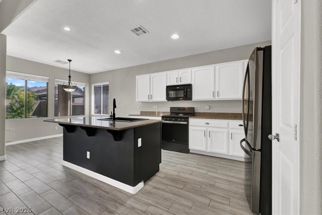 A spacious kitchen presents a dark central island, clean cabinetry, and handsome wood-look tile flooring.