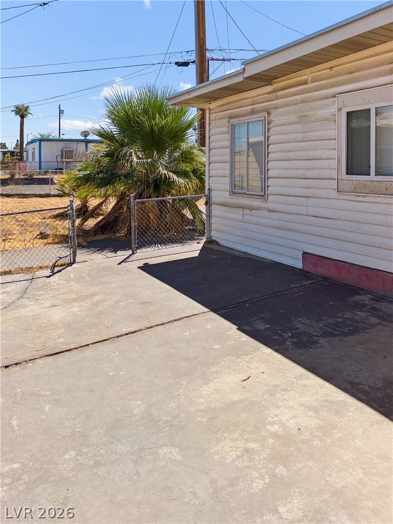 107 W Victory Road, Henderson, NV 89015 Concrete patio area borders the home exterior alongside a fenced yard and mature palm trees.