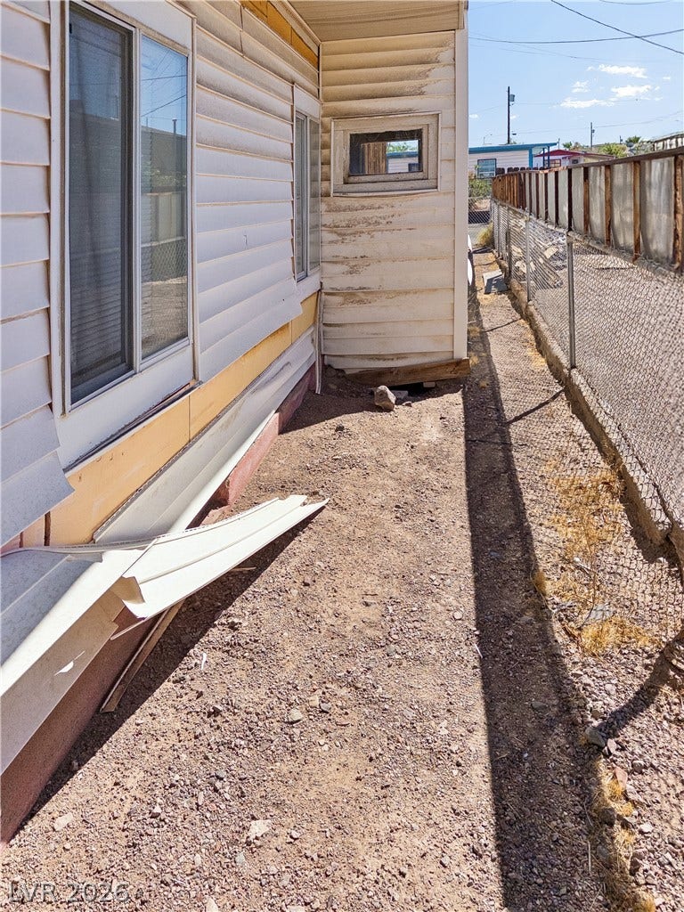 107 W Victory Road, Henderson, NV 89015 A narrow side yard features horizontal siding and chain-link fencing under a bright sky.