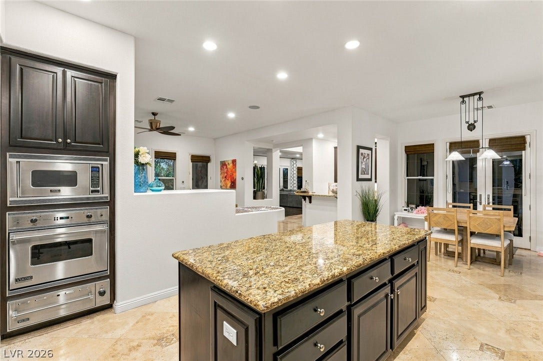 12056 Royal Dolnoch Court, Las Vegas, NV 89141 Gleaming stone countertops and dark cabinetry anchor this open-concept culinary space.