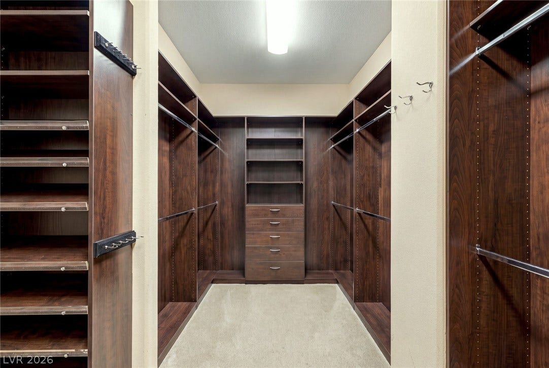 12056 Royal Dolnoch Court, Las Vegas, NV 89141 Rich wood built-ins and soft carpeting define this organized walk-in closet space.