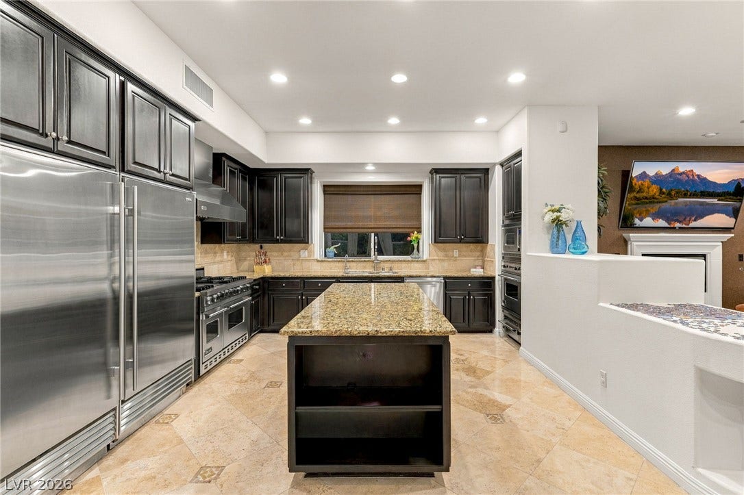 12056 Royal Dolnoch Court, Las Vegas, NV 89141 Gleaming stone countertops and dark cabinetry anchor this kitchen space under recessed lighting.