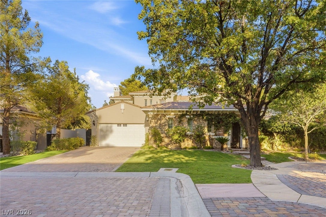 12056 Royal Dolnoch Court, Las Vegas, NV 89141 Mature trees frame a classic stone and stucco facade with a paved driveway.
