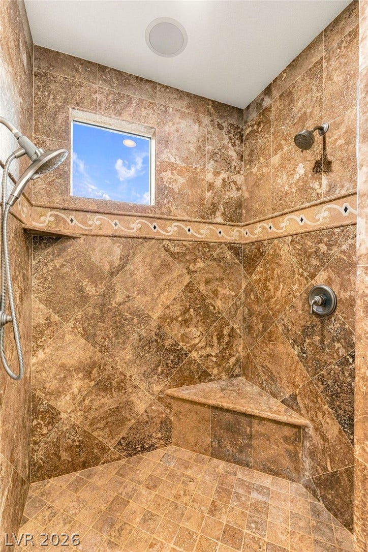 12056 Royal Dolnoch Court, Las Vegas, NV 89141 Ornate natural stone tiling accents this walk-in shower with a built-in corner bench seat.