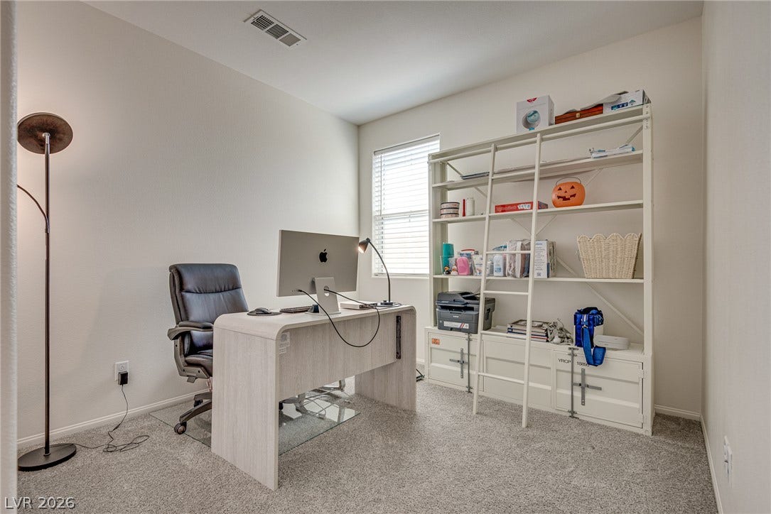 An airy workspace enjoys carpeted flooring and natural light from a large window.