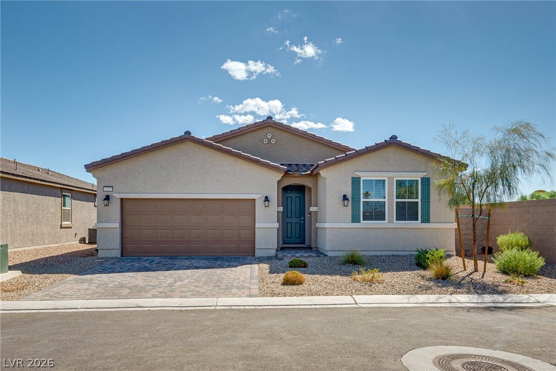 A modern stucco facade features low-maintenance desert landscaping and a brick paver driveway.