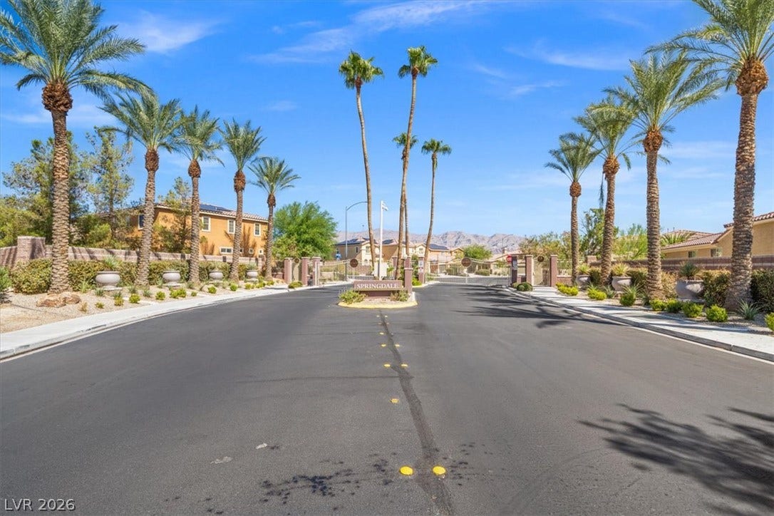 1874 Nature Park Drive, North Las Vegas, NV 89084 Palm trees frame the paved neighborhood street leading toward the gated entry gates.