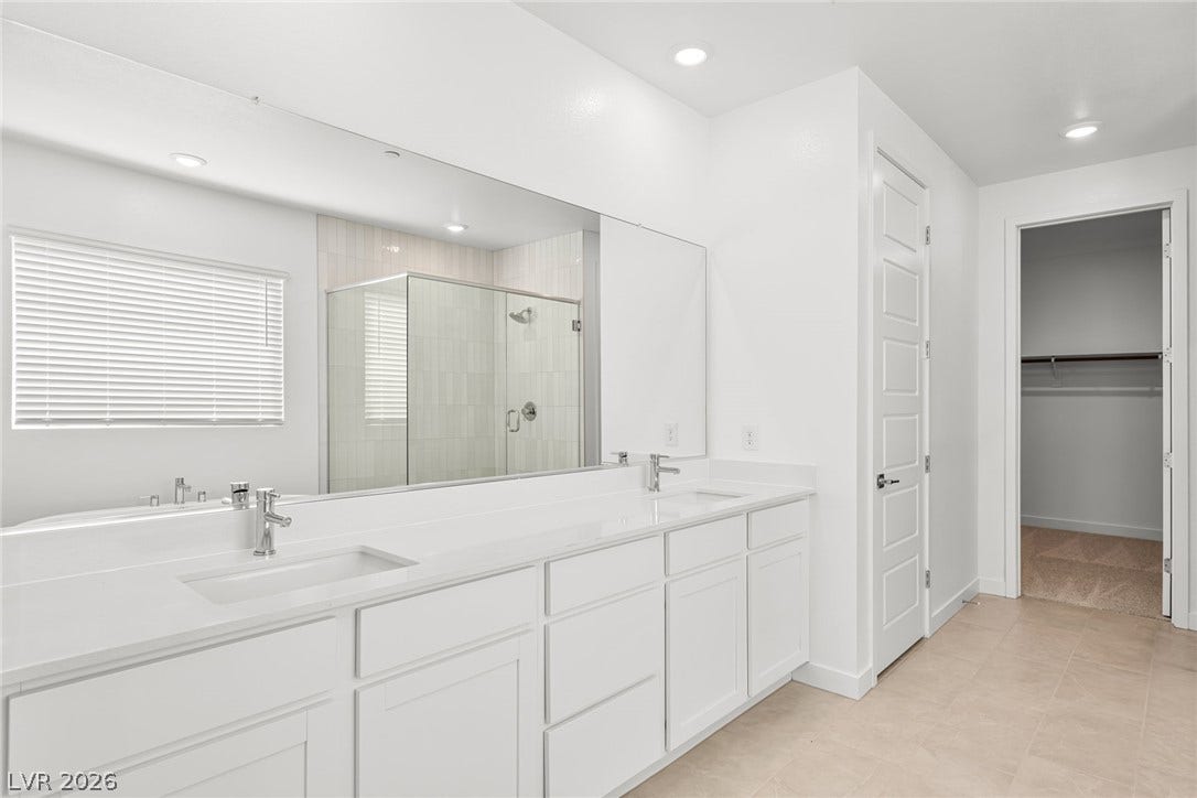 A pristine primary bathroom features dual vanities, a spacious glass-enclosed shower, and a large soaking tub.