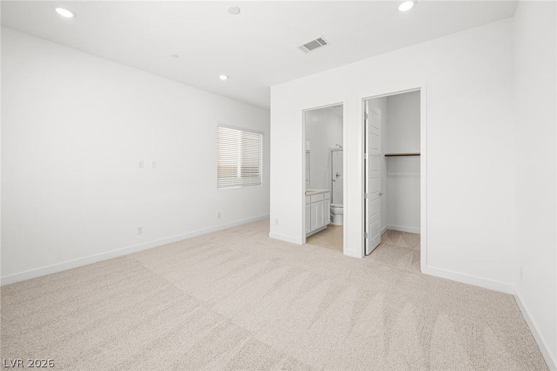 A spacious, naturally illuminated room featuring plush carpeting, window blinds, and convenient access to an en-suite bathroom and walk-in closet.