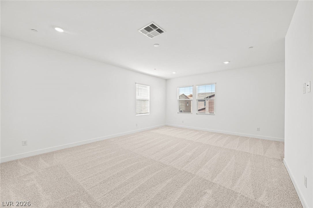 A spacious, naturally illuminated room features plush carpet and recessed lighting.